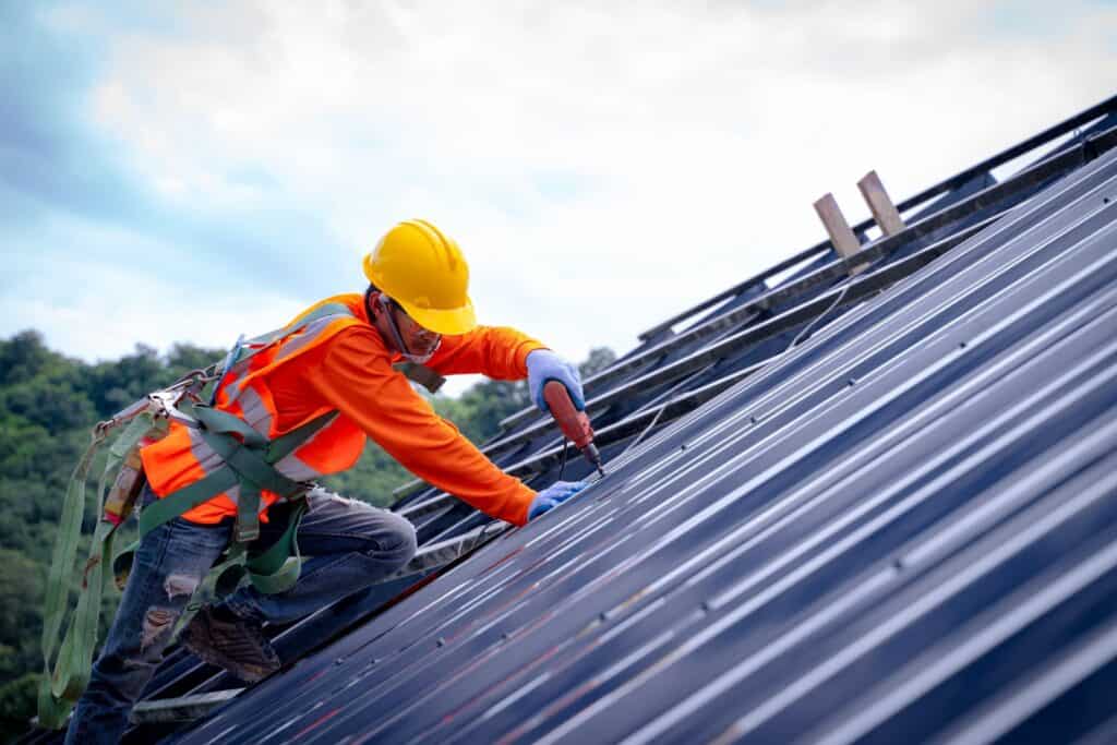 oofer worker in protective uniform wear and gloves, using air or pneumatic nail gun and installing asphalt shingle on top of the new roof, of commercial building under construction.